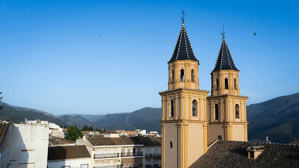 Church towers with yellow facade and black spires against a blue sky.