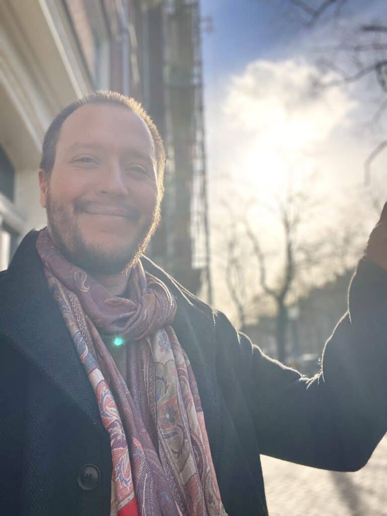 Outdoor portrait of a smiling man with sunlight behind, representing Garden of Light Productions.