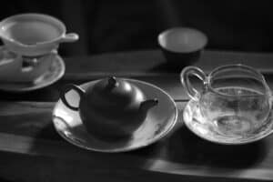 Tea set on wooden table with cups and teapot, black and white image.
