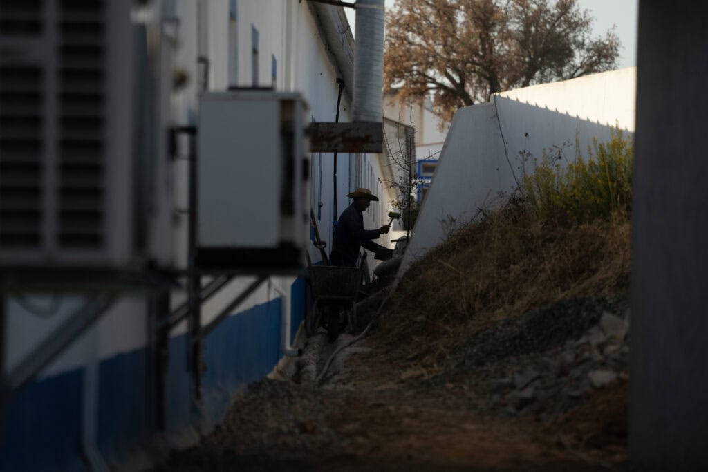 Worker installing outdoor lighting along building exterior at dusk.
