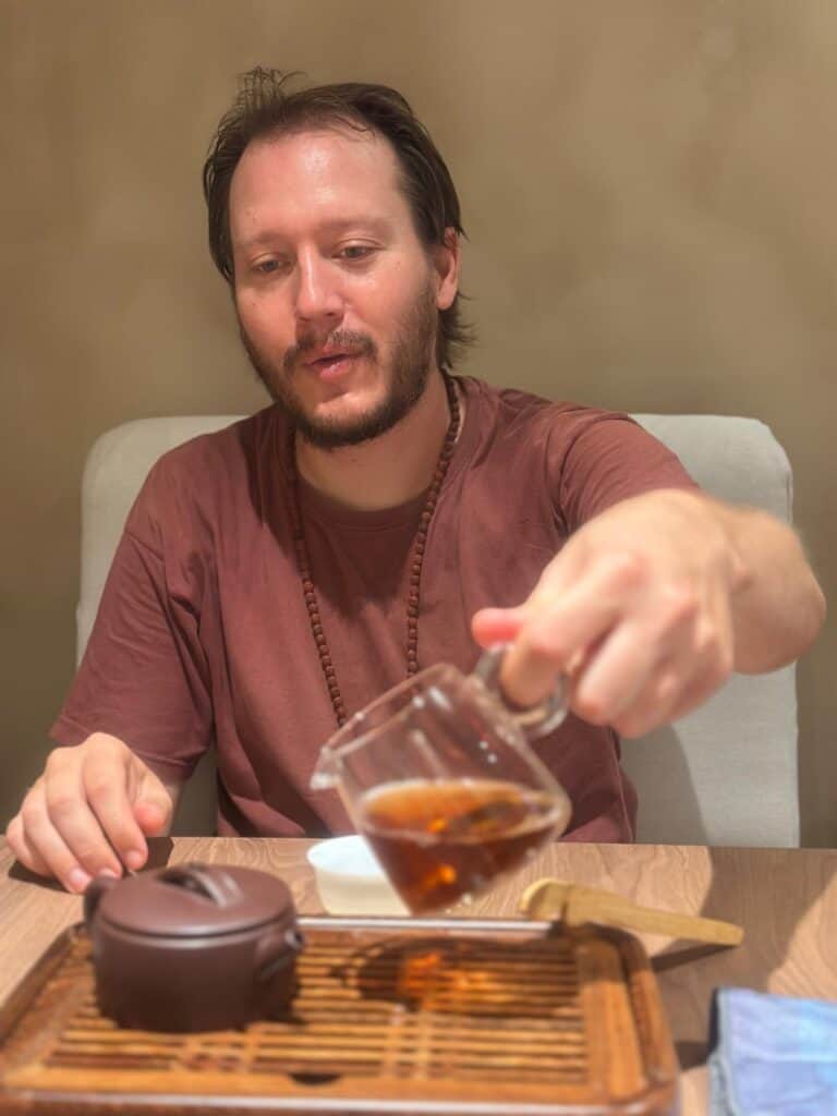 Man pouring tea into a cup at a cozy indoor setting.